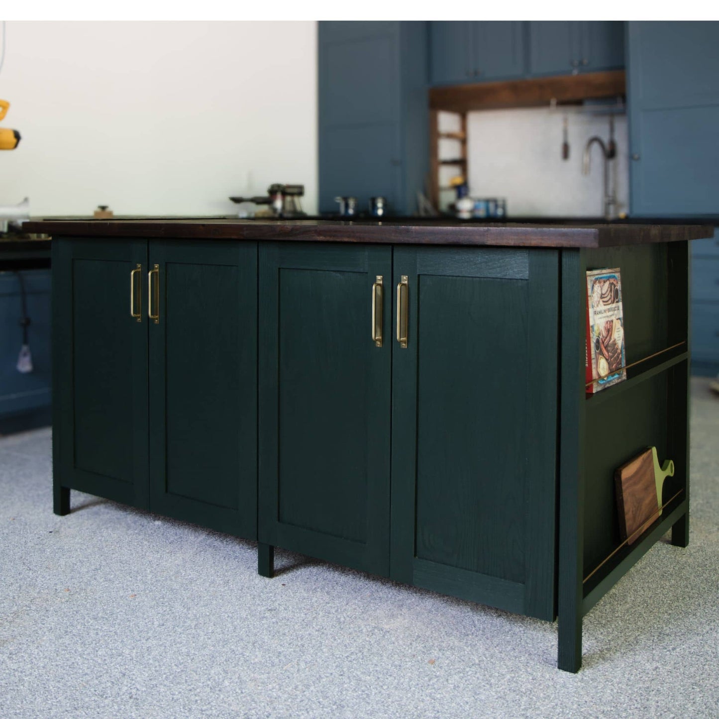 DIY kitchen island stained dark green with a display shelf for cookbooks and cutting boards