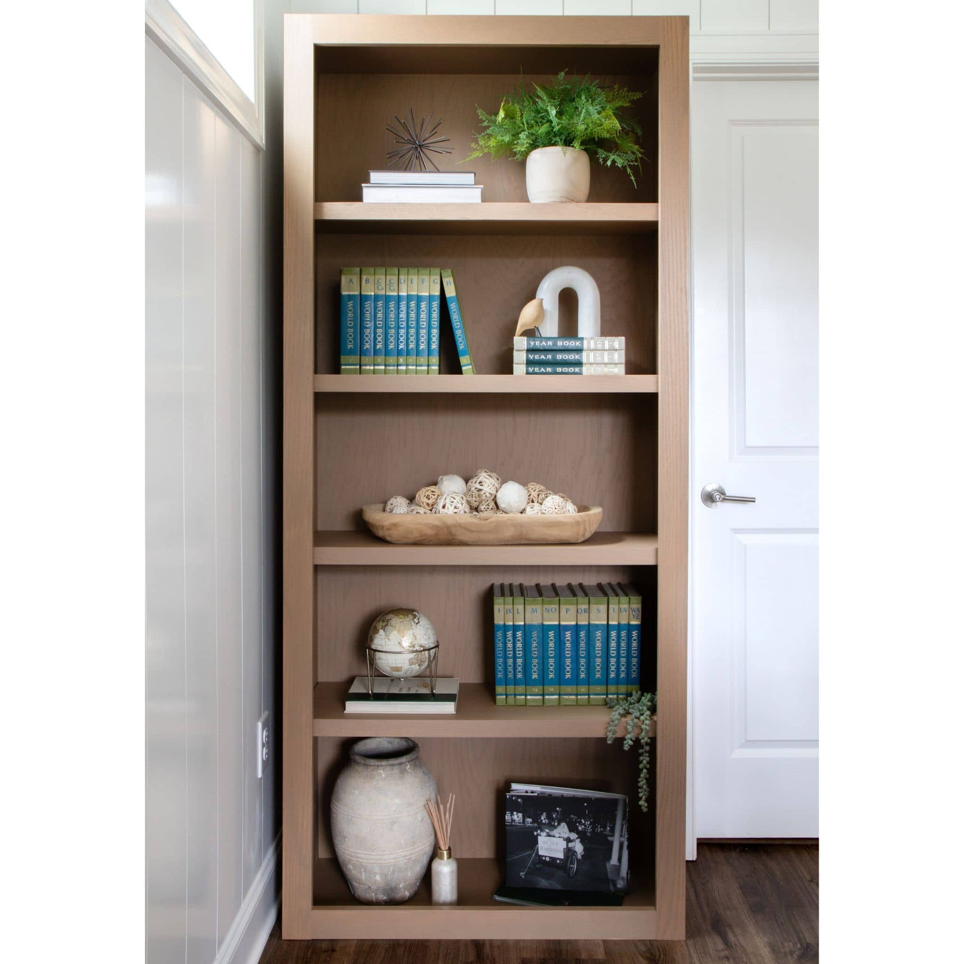 Wooden bookshelf with decorative items in a room with white walls and wooden floor.