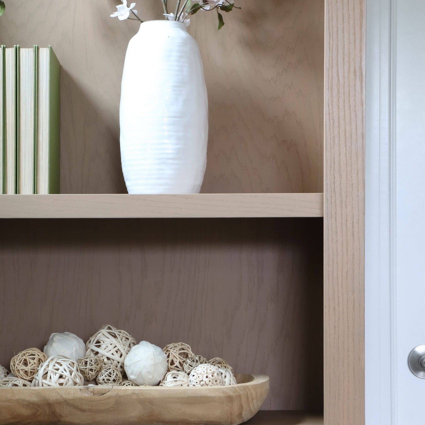 White vase on a wooden shelf with decorative items below