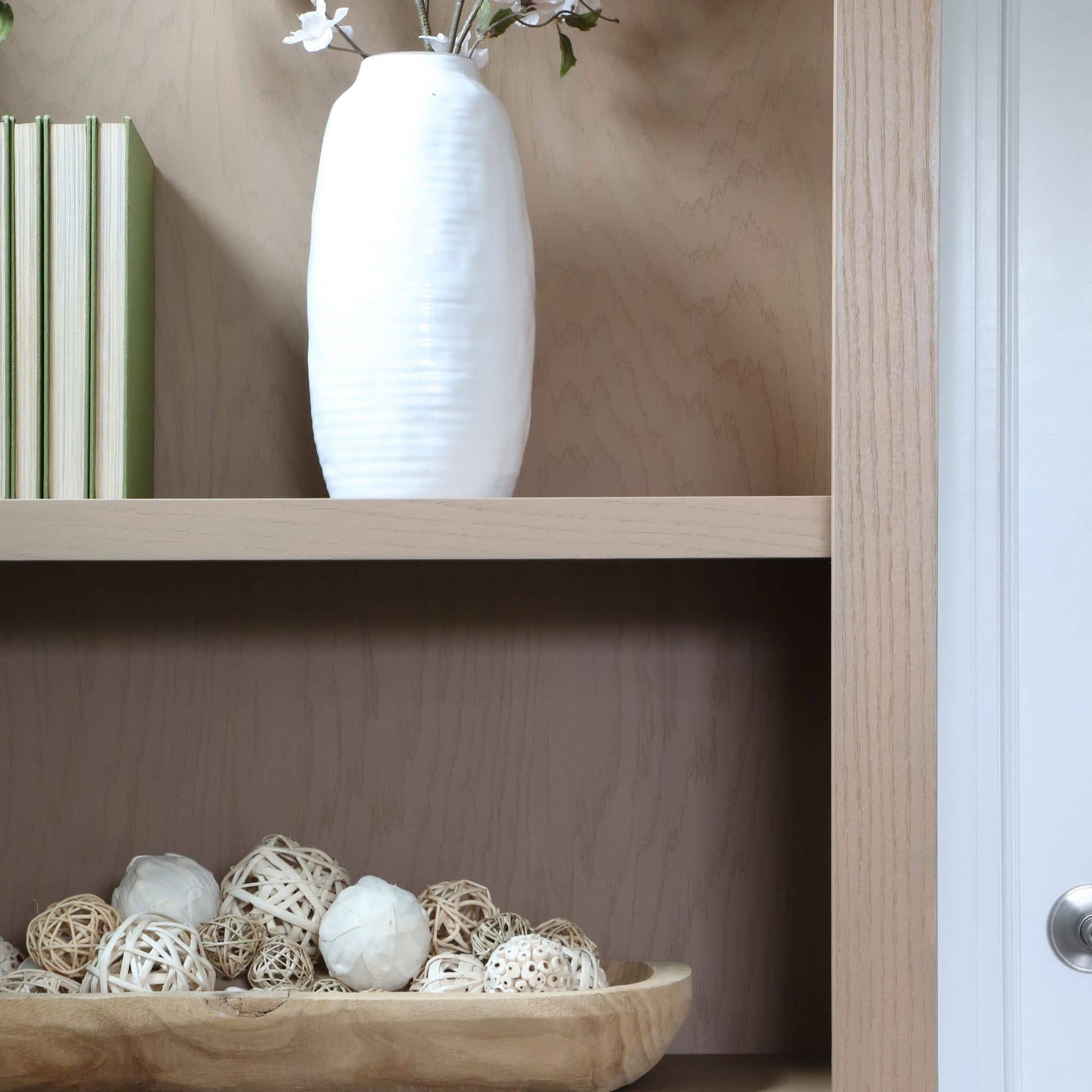 White vase on a wooden shelf with decorative items below